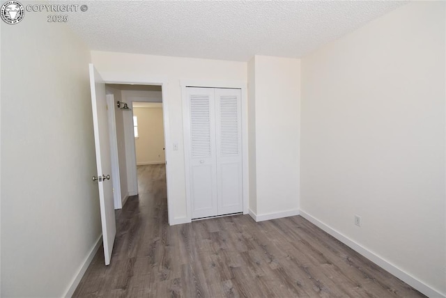 unfurnished bedroom with a closet, a textured ceiling, baseboards, and wood finished floors
