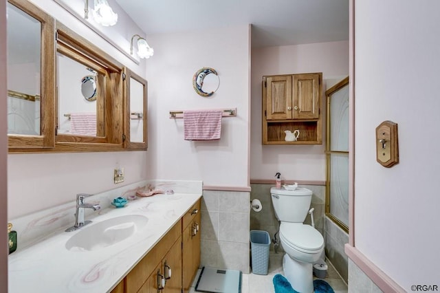 full bathroom with bath / shower combo with glass door, tile walls, vanity, toilet, and tile patterned floors