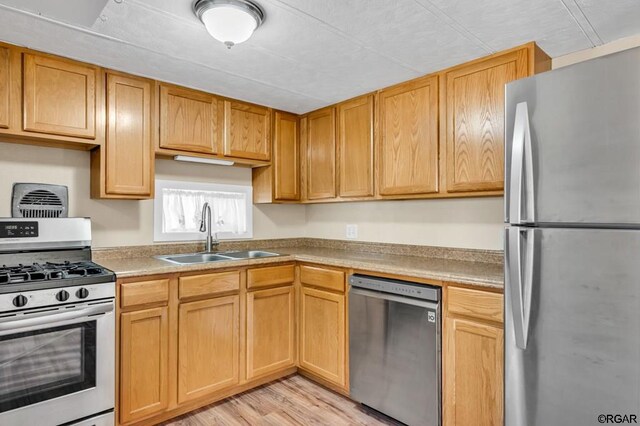 kitchen with appliances with stainless steel finishes, sink, and light wood-type flooring