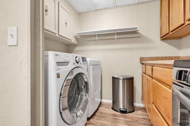 clothes washing area with washing machine and dryer and light wood-type flooring