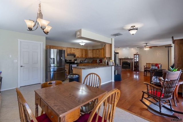 dining room featuring a tiled fireplace, ceiling fan with notable chandelier, and light tile patterned floors