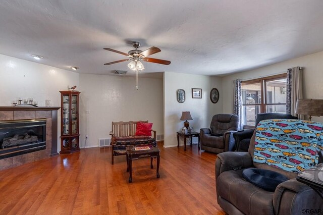 living room featuring a tiled fireplace, hardwood / wood-style floors, and ceiling fan