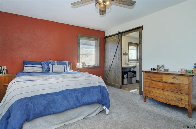 carpeted bedroom with a barn door and ceiling fan