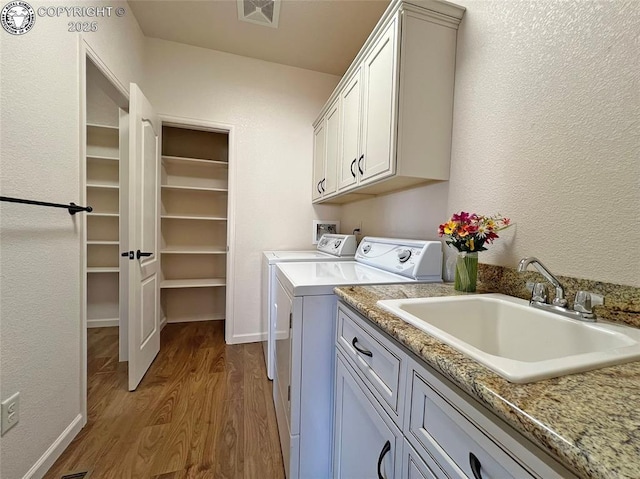 laundry room featuring light wood finished floors, cabinet space, visible vents, washing machine and clothes dryer, and a sink