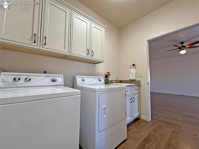 clothes washing area with cabinet space, a ceiling fan, wood finished floors, washer and dryer, and a sink