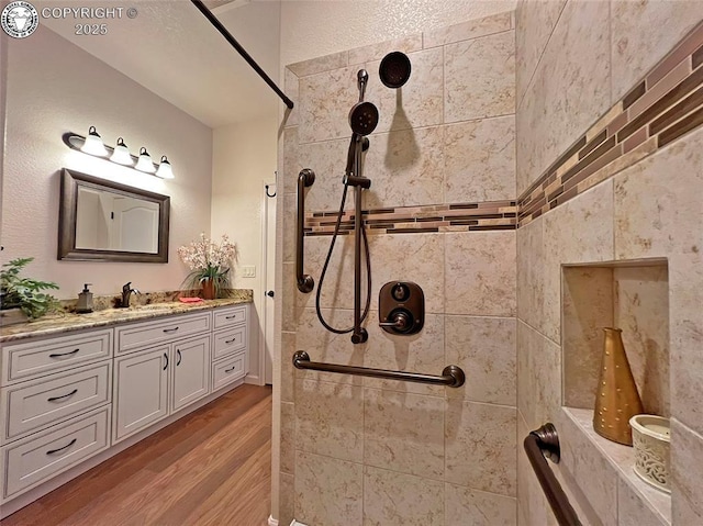 full bath with a tile shower, wood finished floors, and vanity