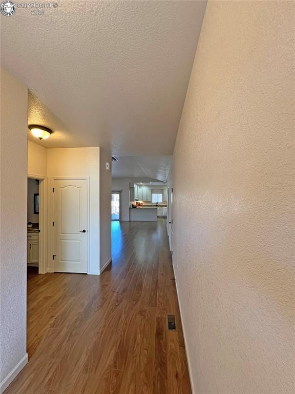 corridor with a textured ceiling, baseboards, dark wood-type flooring, and a textured wall