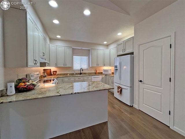 kitchen with white appliances, a peninsula, light stone countertops, under cabinet range hood, and a sink