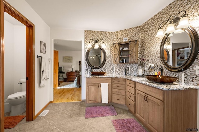 bathroom featuring tile patterned flooring, toilet, vanity, and decorative backsplash