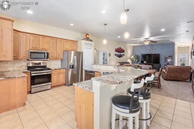 kitchen featuring appliances with stainless steel finishes, pendant lighting, backsplash, light tile patterned floors, and light stone countertops