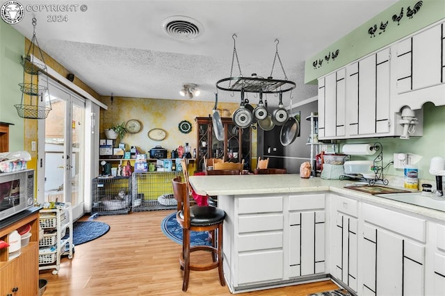 kitchen featuring a textured ceiling, light hardwood / wood-style flooring, kitchen peninsula, and white cabinets