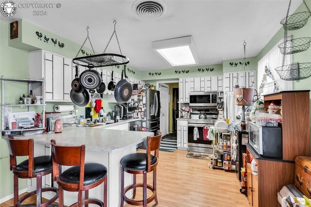 kitchen with a breakfast bar, white cabinetry, light hardwood / wood-style flooring, kitchen peninsula, and stainless steel appliances