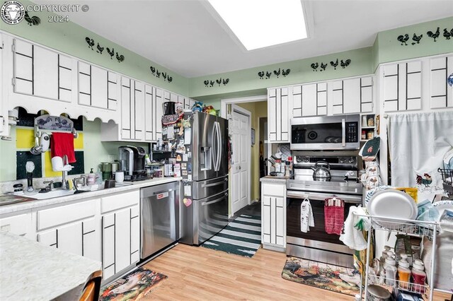 kitchen with a skylight, light wood-type flooring, white cabinets, and appliances with stainless steel finishes