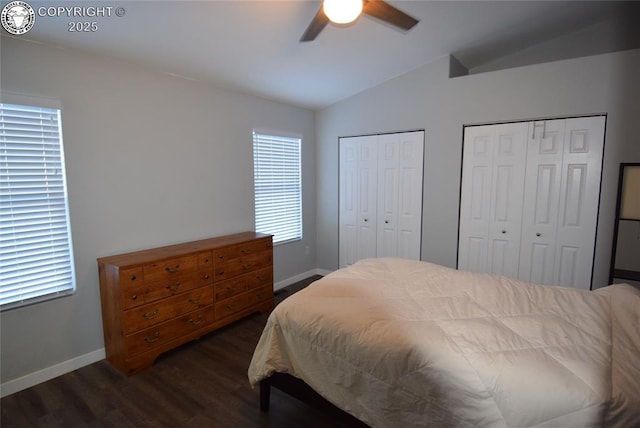 bedroom with lofted ceiling, two closets, dark wood-type flooring, and ceiling fan