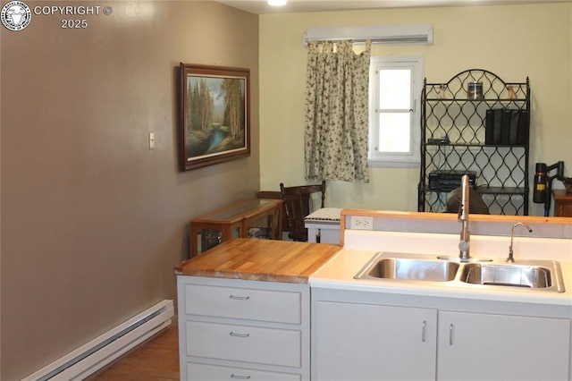 kitchen featuring a baseboard heating unit, a sink, white cabinetry, light countertops, and a wall mounted air conditioner