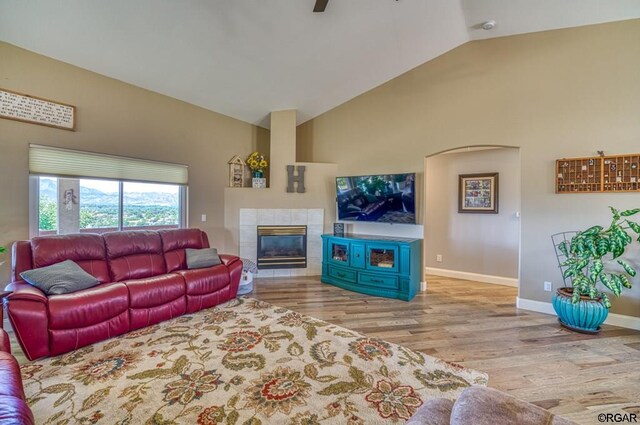 living room featuring a fireplace, light hardwood / wood-style flooring, ceiling fan, and vaulted ceiling