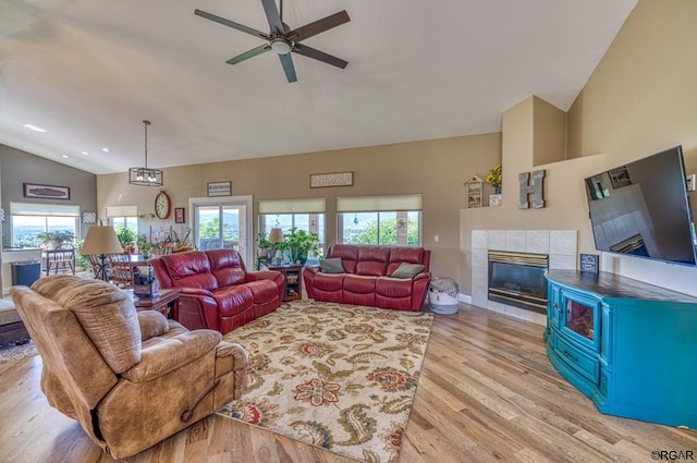 living room featuring ceiling fan, lofted ceiling, a tiled fireplace, and light wood-type flooring