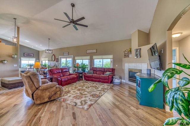 living room featuring ceiling fan, high vaulted ceiling, a tile fireplace, and light hardwood / wood-style flooring