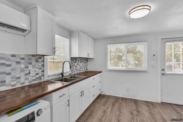 kitchen featuring sink, white cabinetry, backsplash, wood counters, and an AC wall unit