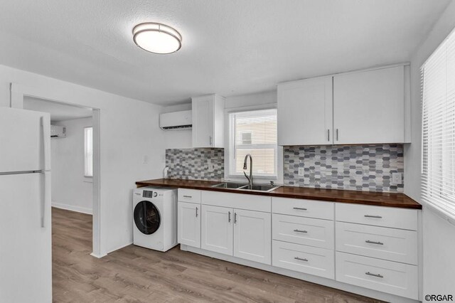 kitchen with butcher block countertops, white cabinetry, washer / dryer, sink, and white fridge