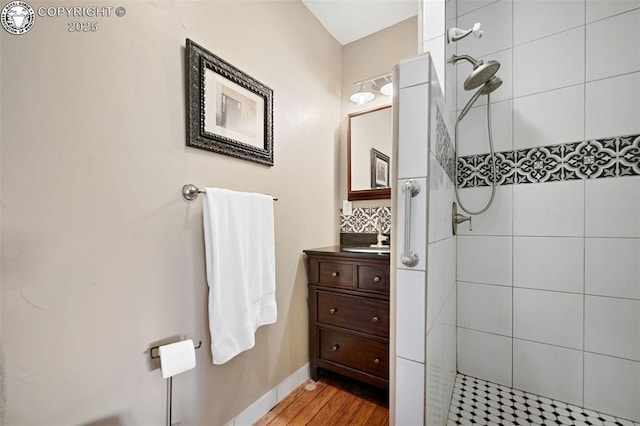 bathroom with wood finished floors, backsplash, a tile shower, and vanity