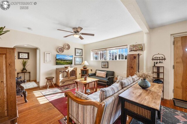 living room with arched walkways, beam ceiling, wood finished floors, and a ceiling fan