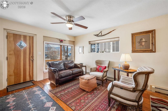 sitting room with a ceiling fan, baseboard heating, and wood finished floors