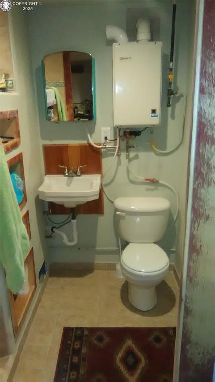 half bath featuring tankless water heater, baseboards, a sink, and toilet