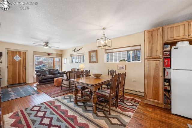 dining area with a textured ceiling, baseboard heating, wood-type flooring, and ceiling fan with notable chandelier