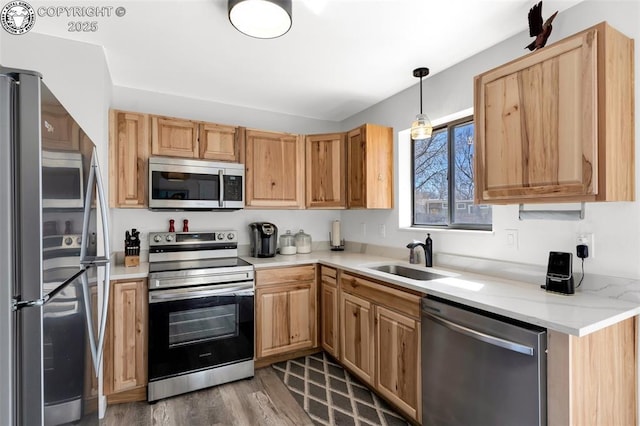 kitchen with appliances with stainless steel finishes, wood finished floors, light brown cabinetry, pendant lighting, and a sink