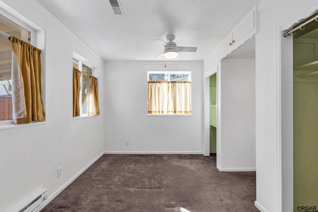 unfurnished room featuring dark colored carpet, a baseboard heating unit, and ceiling fan