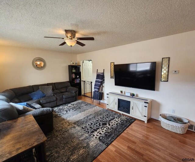 living room featuring hardwood / wood-style flooring, ceiling fan, and a textured ceiling