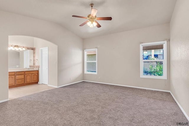 unfurnished bedroom with connected bathroom, sink, light colored carpet, vaulted ceiling, and ceiling fan