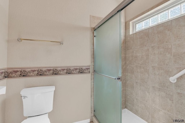 bathroom featuring a shower with door and toilet