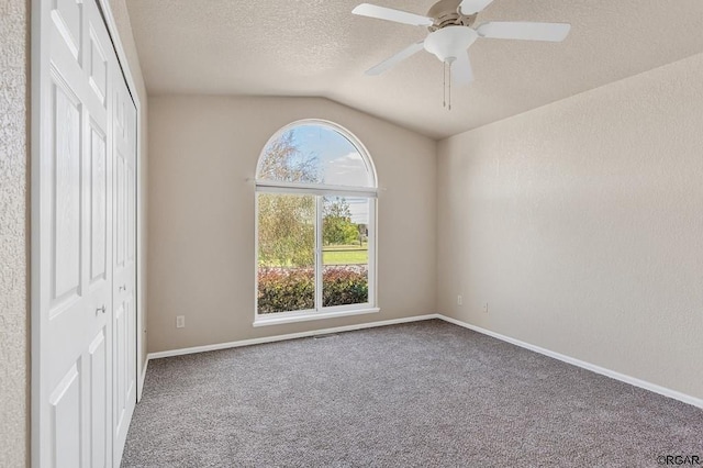 carpeted spare room featuring a textured ceiling, vaulted ceiling, and ceiling fan