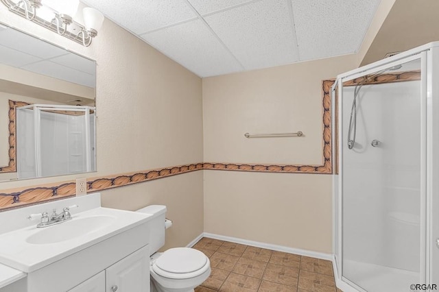 bathroom with a drop ceiling, an enclosed shower, vanity, and toilet