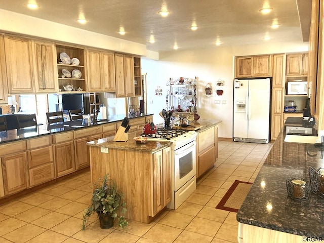 kitchen featuring light tile patterned flooring, a center island, white appliances, and dark stone counters