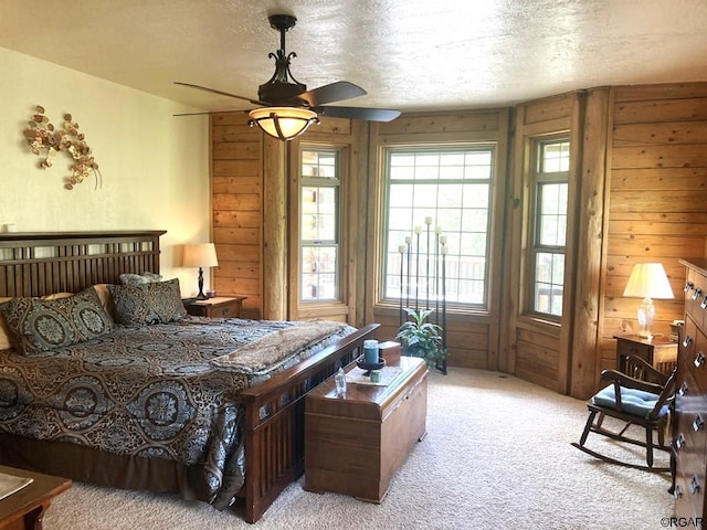 carpeted bedroom featuring a textured ceiling, ceiling fan, and wood walls