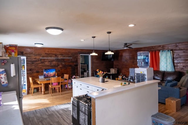 kitchen with stainless steel refrigerator, wood walls, decorative light fixtures, ceiling fan, and light hardwood / wood-style flooring