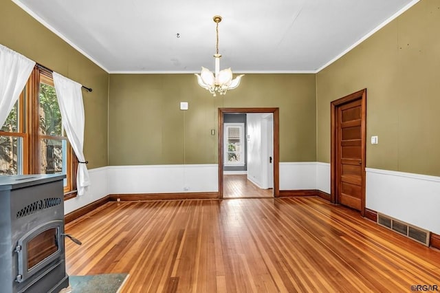 unfurnished dining area featuring visible vents, ornamental molding, hardwood / wood-style floors, a wood stove, and an inviting chandelier