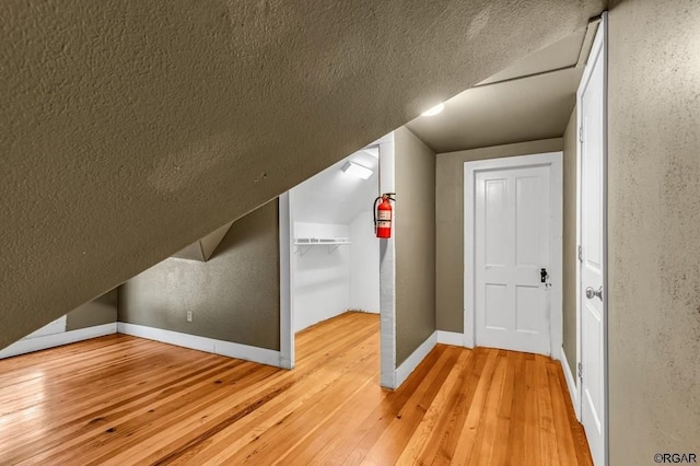 bonus room featuring light wood finished floors, baseboards, and a textured ceiling