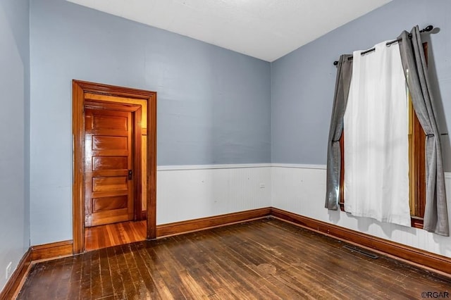 empty room with a wainscoted wall, visible vents, baseboards, and hardwood / wood-style flooring