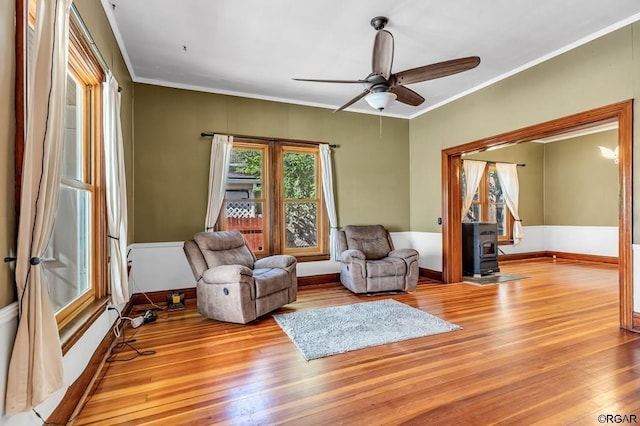 living area with a wood stove, light wood-style floors, baseboards, and crown molding