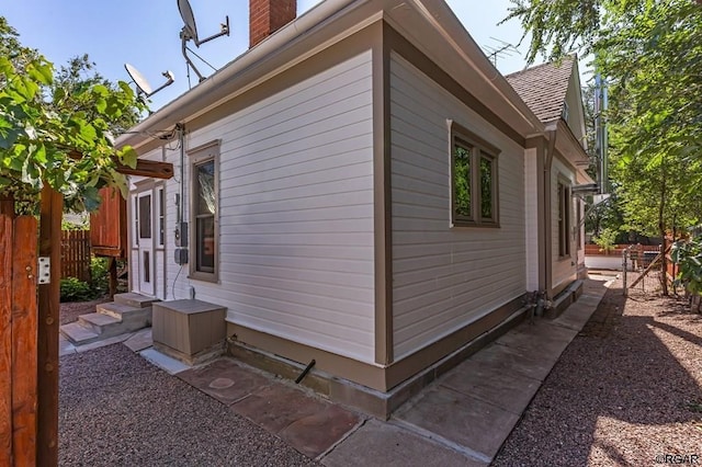 view of side of home with entry steps, fence, and a chimney