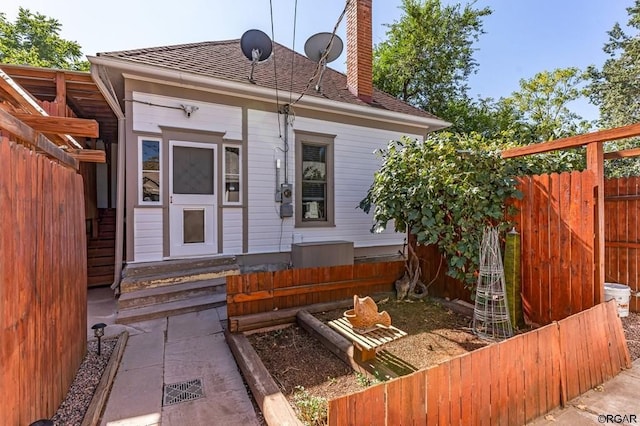 rear view of property featuring roof with shingles, a chimney, and fence