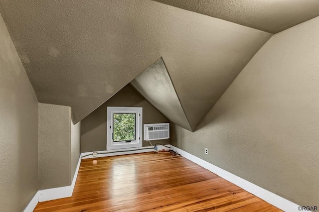 bonus room featuring vaulted ceiling, light wood-style flooring, baseboards, and a wall mounted AC