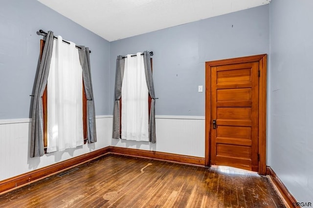 unfurnished room featuring visible vents, hardwood / wood-style floors, and wainscoting