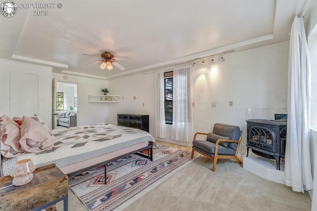 bedroom with track lighting, a wood stove, a ceiling fan, and light carpet