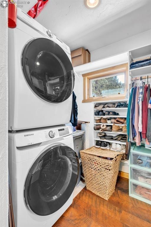 clothes washing area with laundry area, stacked washer and clothes dryer, and wood finished floors