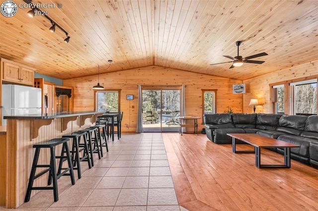 living room with wooden walls, light tile patterned floors, lofted ceiling, rail lighting, and wooden ceiling